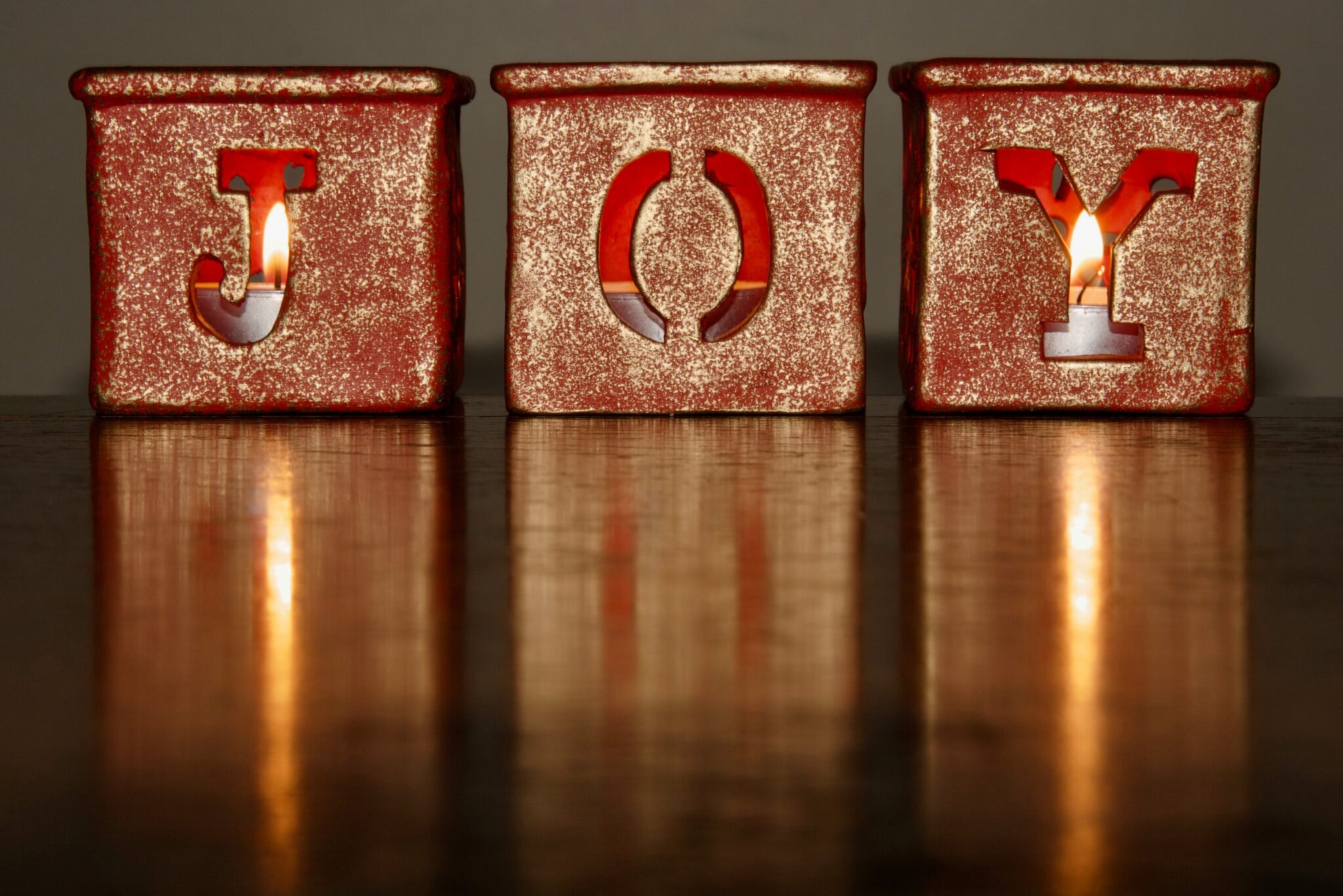 Three gold blocks with the letters J O Y on them against a dark background.