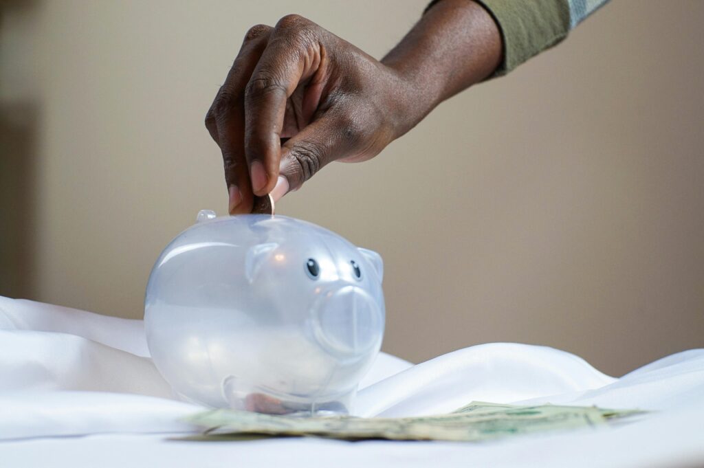 Close up of a hand putting a coin into a white piggy bank.