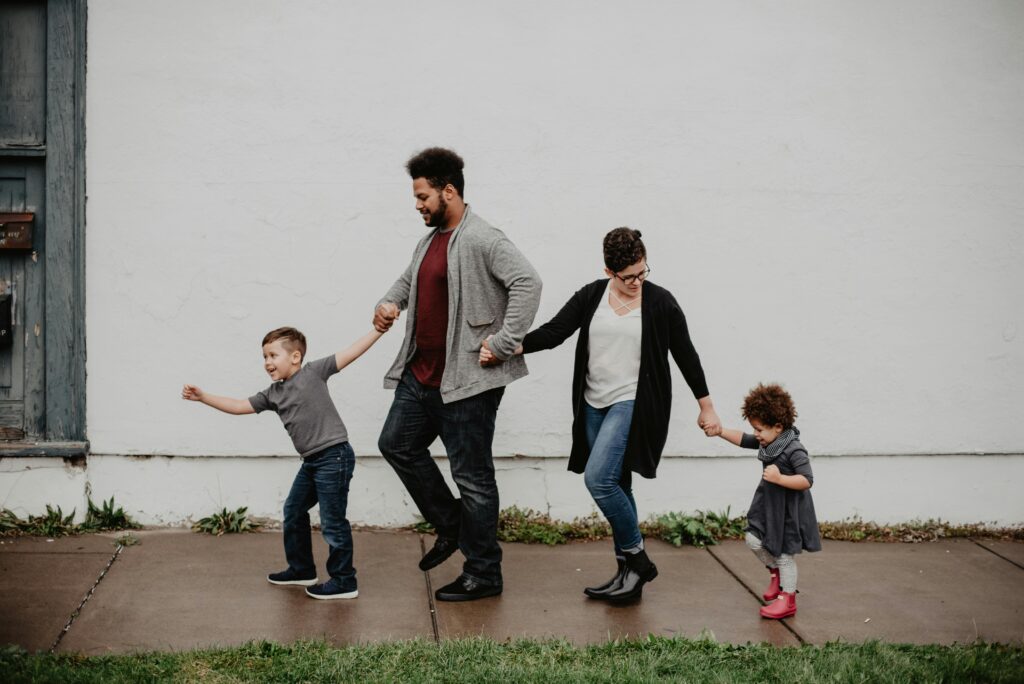 A man, woman, and two small children holding hands in a line, taking a walk.