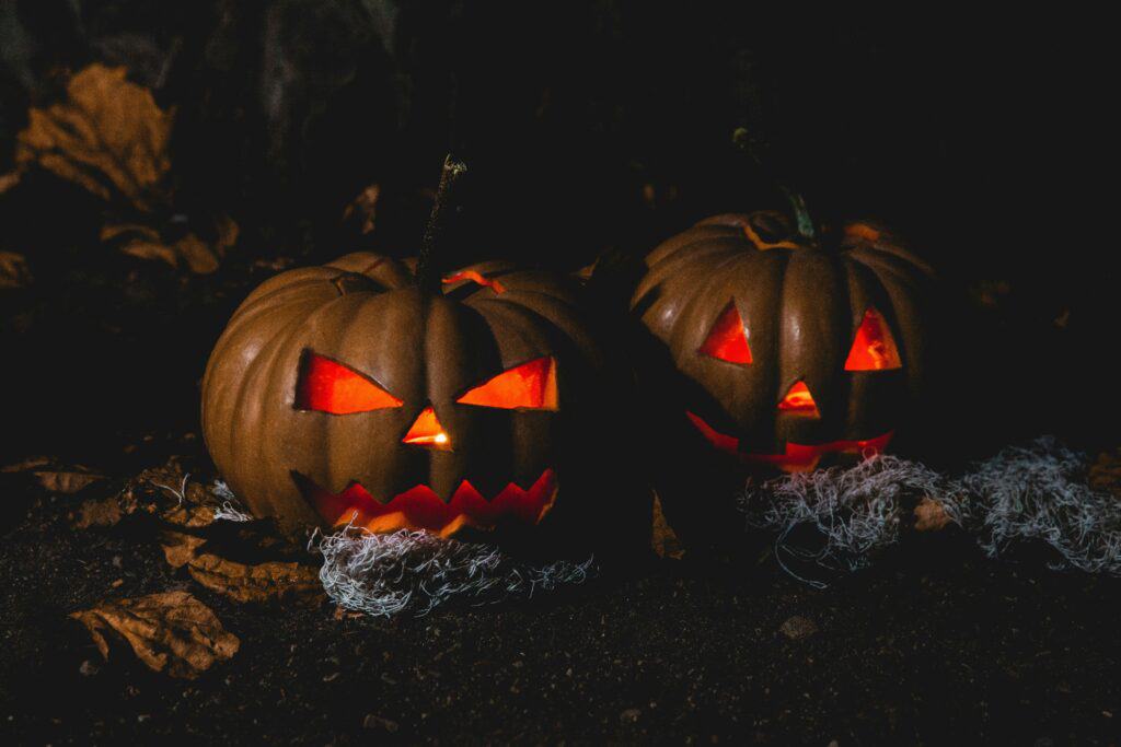 Dark background with two carved Halloween pumpkins glowing orange on the inside.